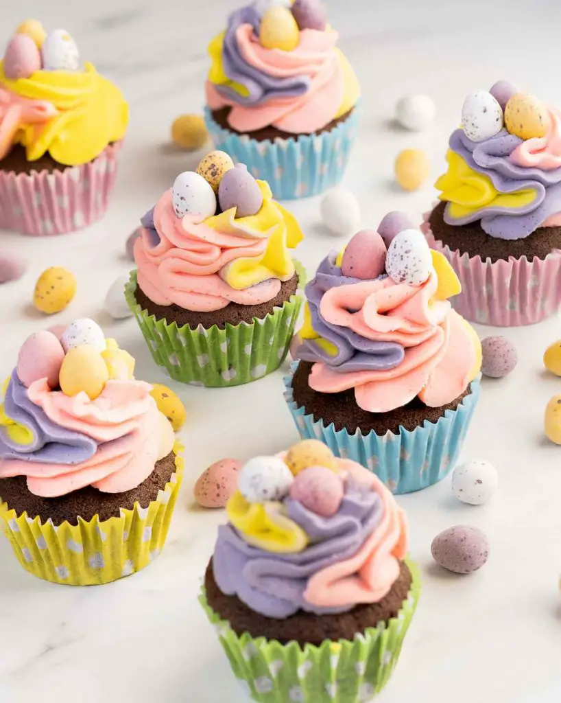 Chocolate cupcakes topped with pink, purple and yellow vanilla buttercream and mini eggs nestled on top. Recipe by movers and bakers