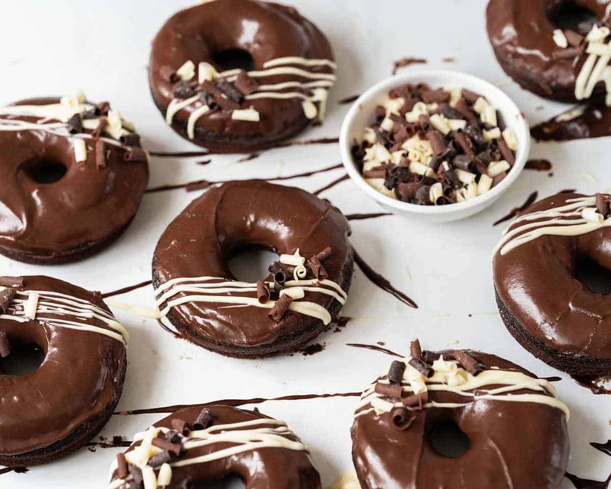 Soft, light and moist chocolate doughnuts with a delicious chocolate fudge glaze, white chocolate drizzle and chocolate curls to finish. Recipe by movers and bakers