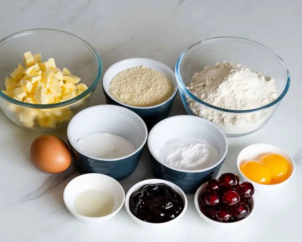 Ingredients for this bake: plain flour, icing sugar, unsalted butter, egg yolks, almond flour, caster sugar, whole egg, almond extract, cherry conserve, milk and glacé cherries. Recipe by movers and bakers