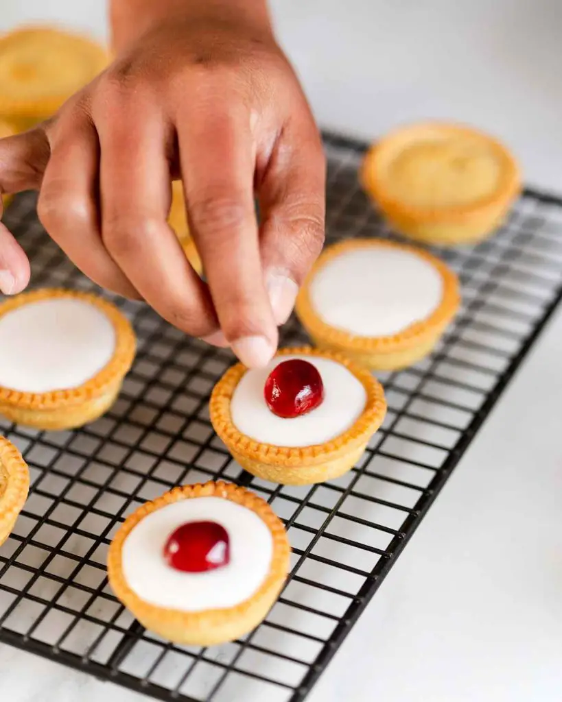 The baked bakewell tarts are finished off with an icing glaze and a glacé cherry half. Are they not just adorable? Recipe by movers and bakers