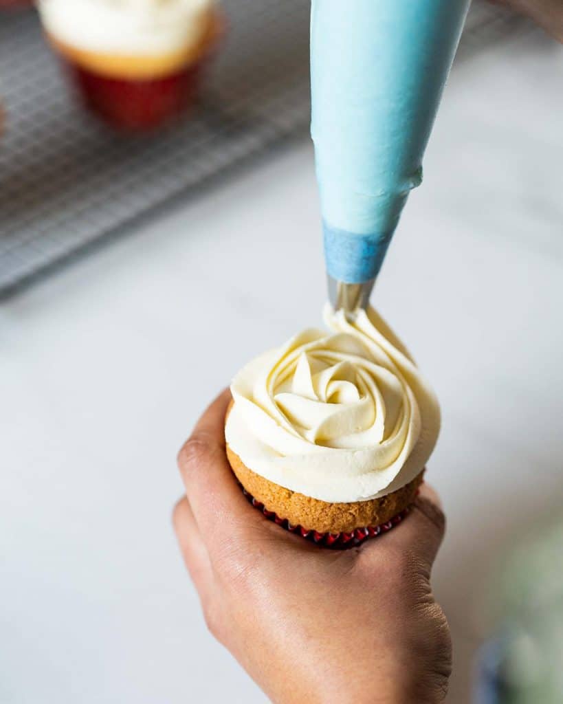 Piping the brandy buttercream over the cupcakes before finishing with some edible silver ball decorations. Recipe by movers and bakers