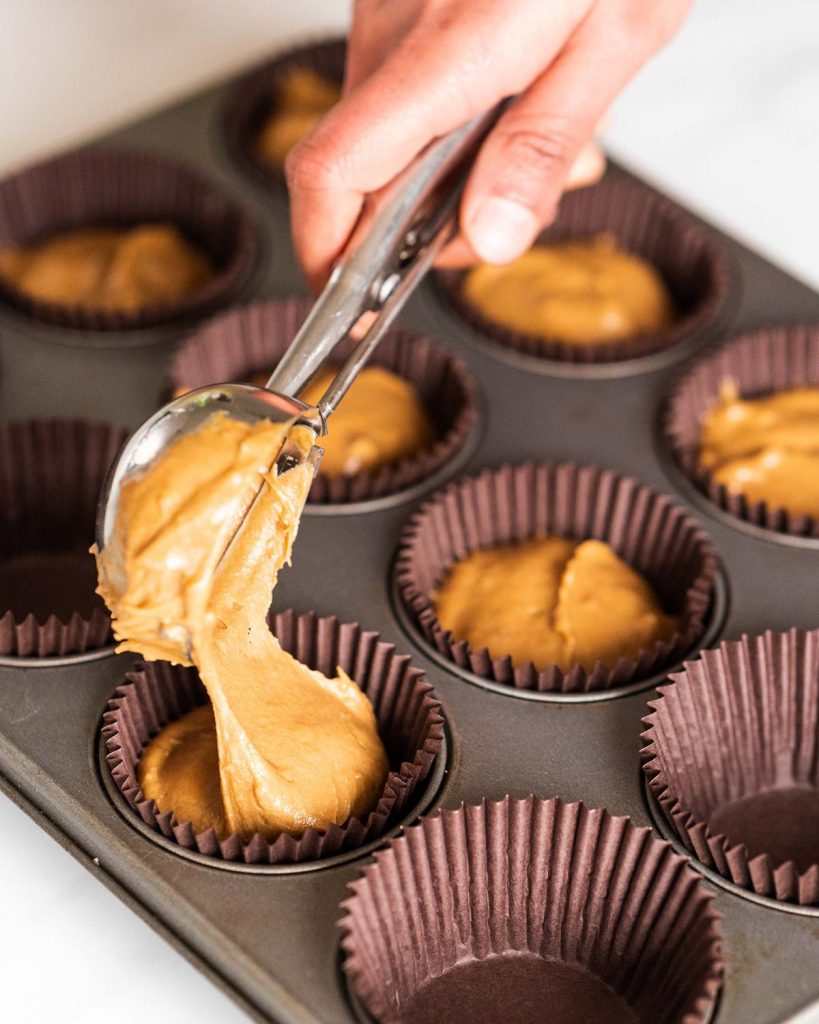 Scooping coffee and walnut cupcake batter into cases before baking.