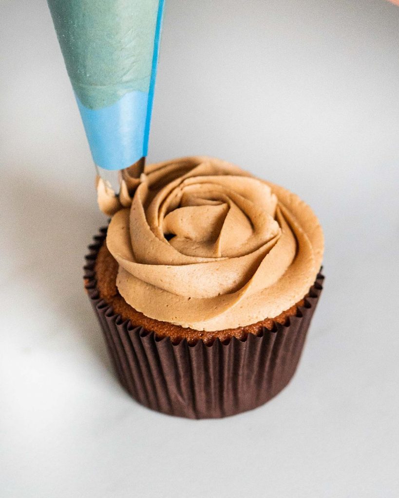 Piping a rosette of coffee buttercream on the cupcakes before adding the final touches