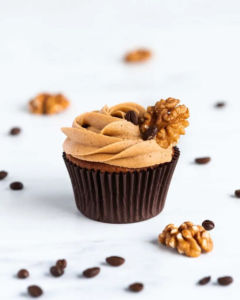Coffee and walnut cupcake with a scattering of coffee beans and walnuts around it.