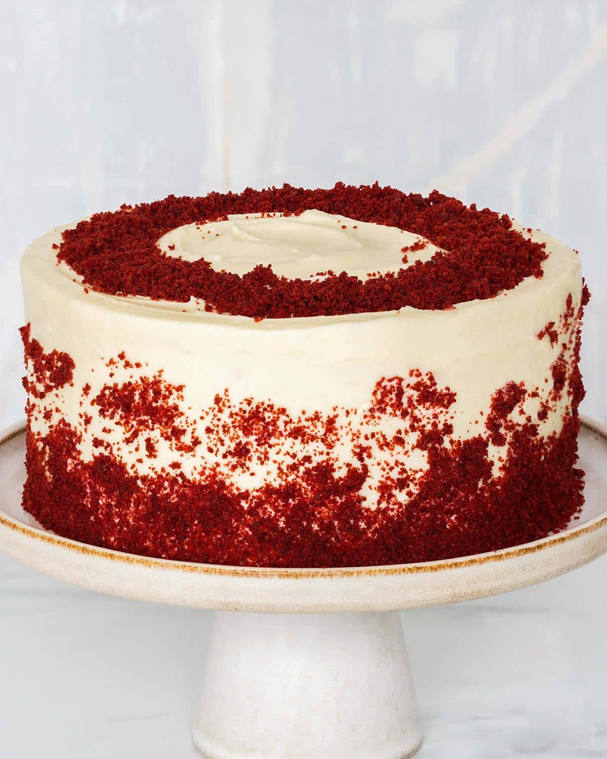 The best eggless red velvet cake recipe. Delicious light chocolate and vanilla flavoured cake layers filled and covered with a beautiful rich cream cheese icing then decorated with red velvet cake crumbs. Recipe by movers and bakers
