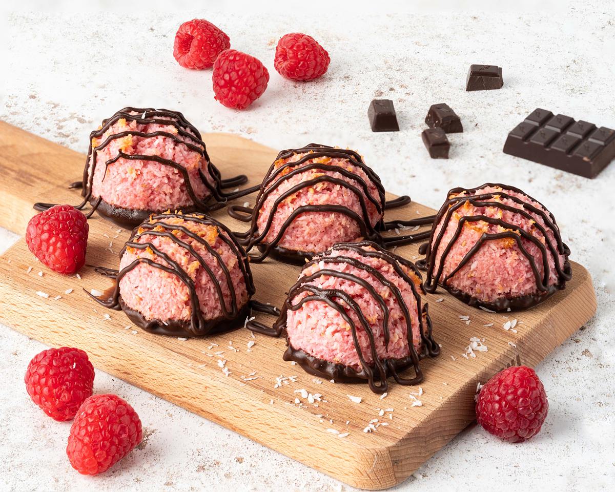 Raspberry chocolate macaroons on a wooden serving board with scattered raspberries and dark chocolate around. Recipe by movers and bakers