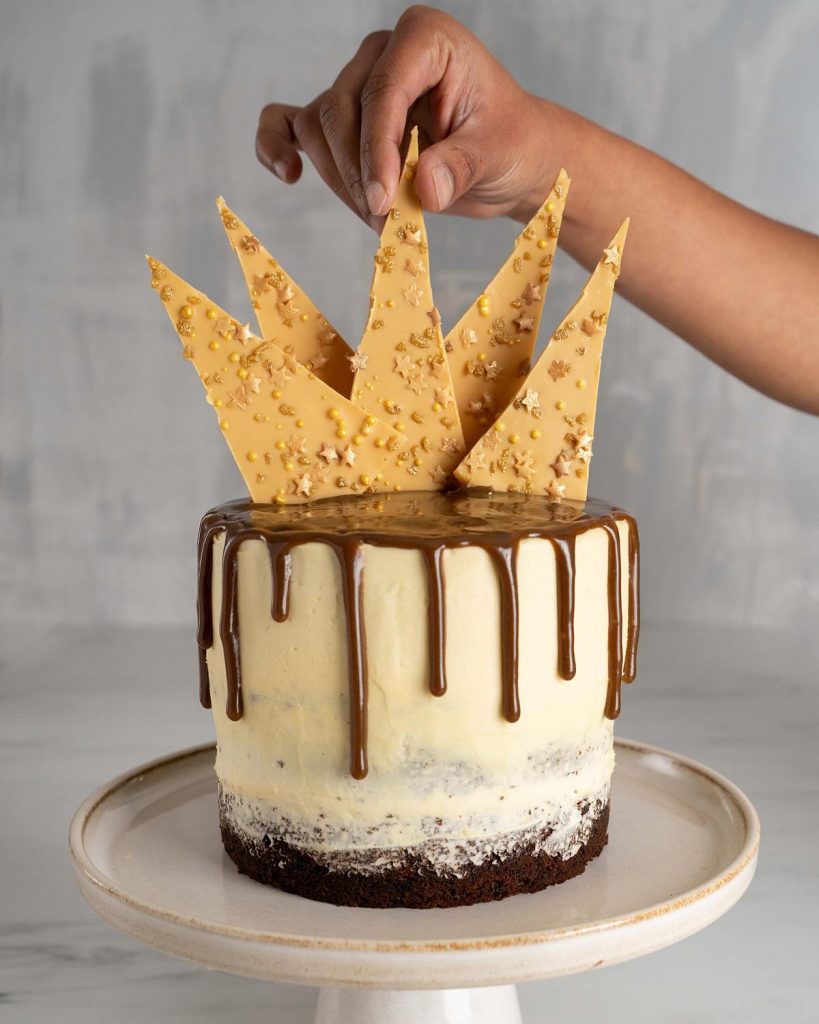 Adding the chocolate shards as the final touch to this spectacular celebration cake! Recipe by movers and bakers