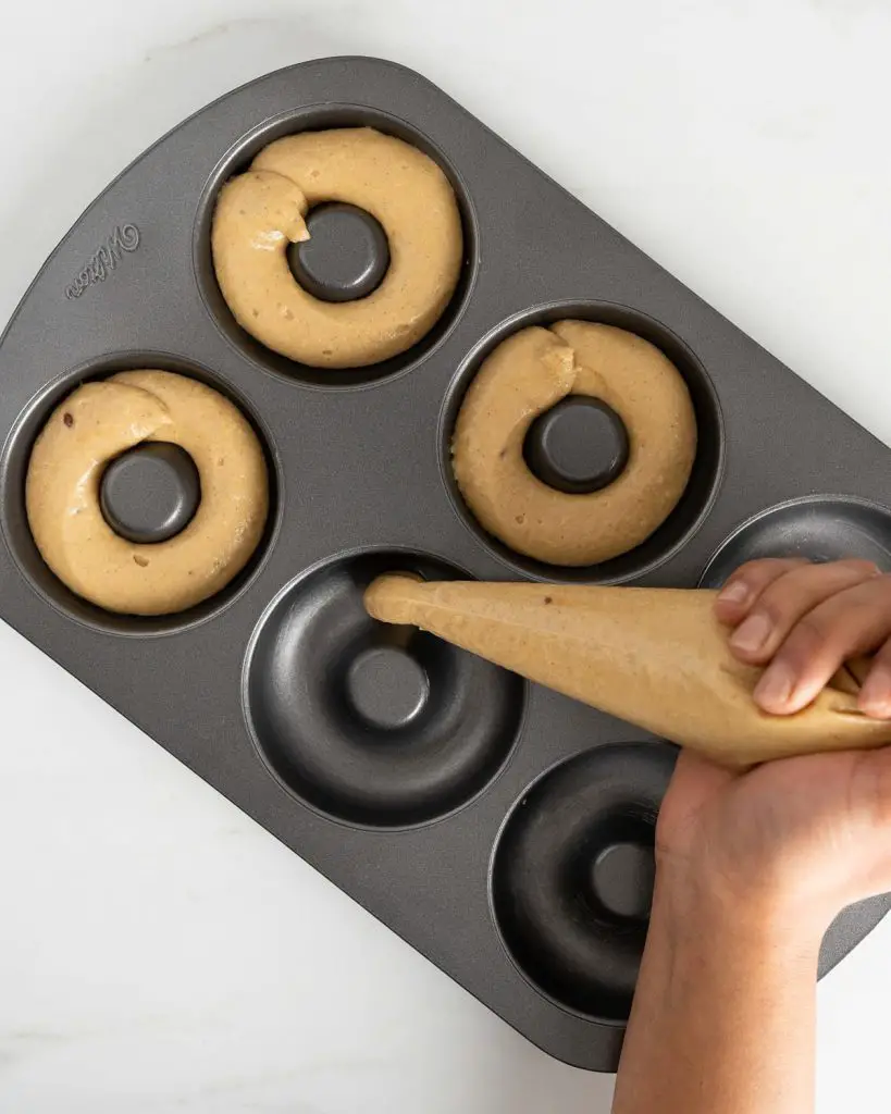 Piping the doughnut batter into the pan before baking. Recipe by movers and bakers