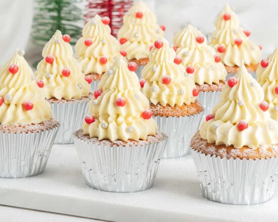 White chocolate Christmas tree cupcakes. Delicious light and fluffy white chocolate cupcakes topped with white chocolate buttercream Christmas trees and sprinkle decorations. Perfect for the festive season! Recipe by movers and bakers