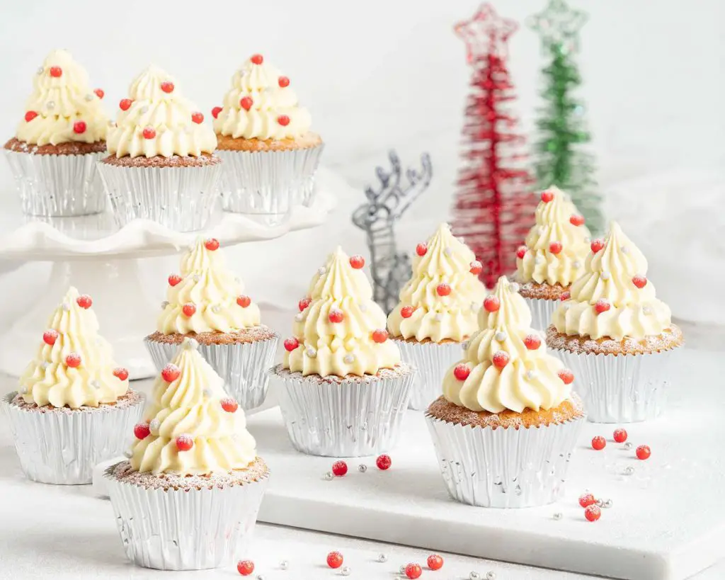 White chocolate Christmas tree cupcakes. Delicious light and fluffy white chocolate cupcakes topped with white chocolate buttercream Christmas trees and sprinkle decorations. Perfect for the festive season! Recipe by movers and bakers