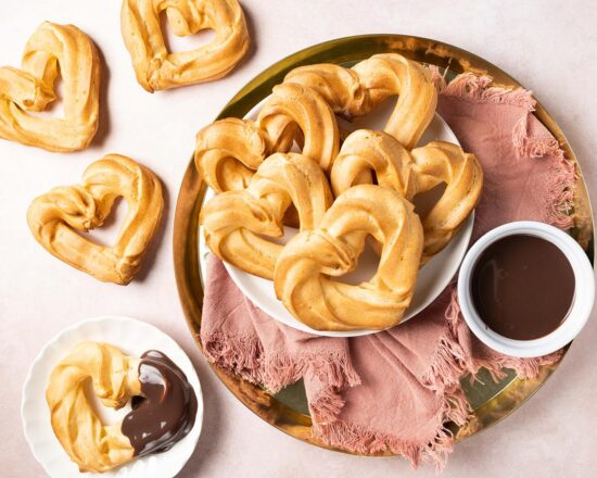 Churros with chocolate sauce. These heart shaped churros are a perfect Valentine's dessert, or just to share with loved ones any time! Churros served with a wonderful rich chocolate fudge sauce makes this an indulgent dessert everyone loves! Recipe by movers and bakers