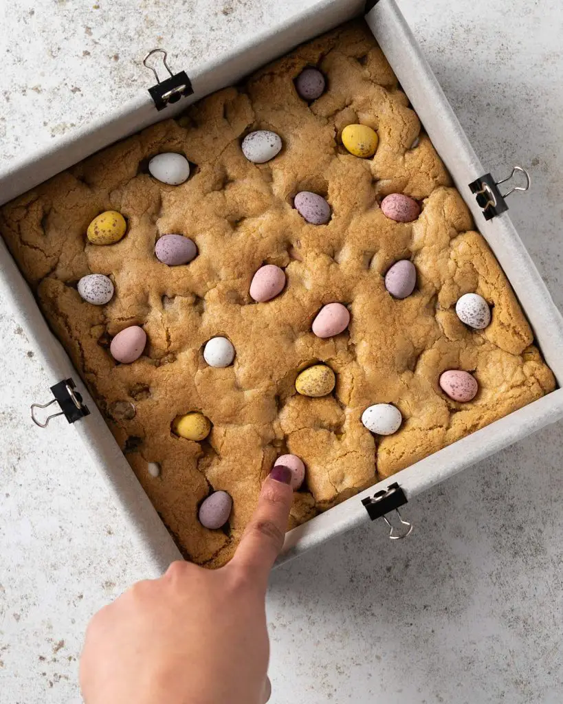 Pressing the reserved chocolate eggs into the cookie as soon as it comes out of the oven. Recipe by movers and bakers
