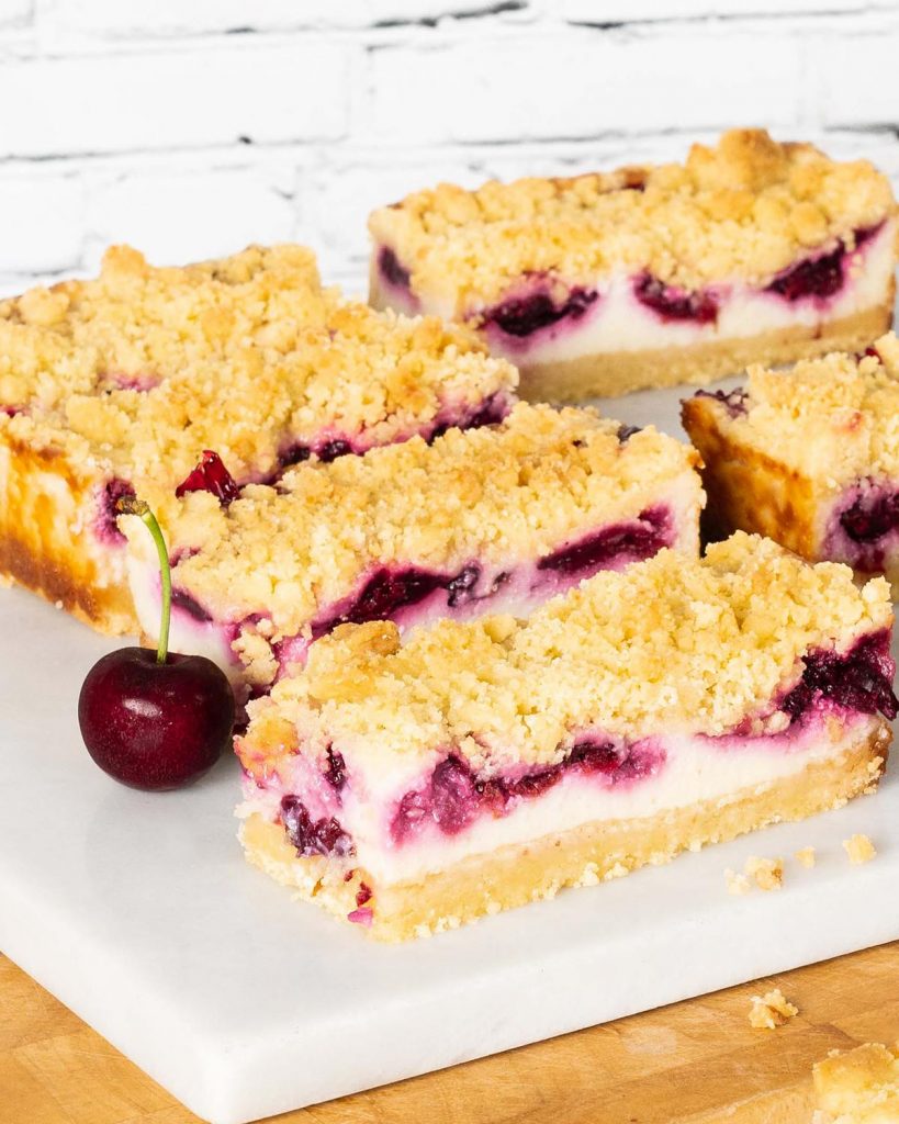 Cherry cheesecake bars. Delicious shortbread, creamy eggless baked cheesecake and rich cherry pie filling topped with more shortbread crumbs. This is one cheesecake no one can turn down! Recipe by movers and bakers