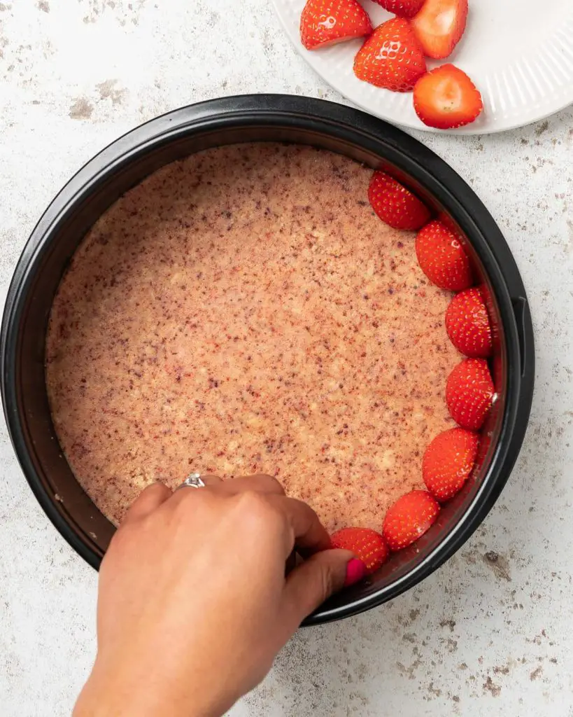 Lining the edge of the tin with the halved strawberries....