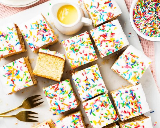 Go for gold with this nostalgic old school cake. A light vanilla traybake cake is topped with simple white icing and plenty of sprinkles. Serve with plenty of custard for the ultimate school dessert treat! Recipe by movers and bakers