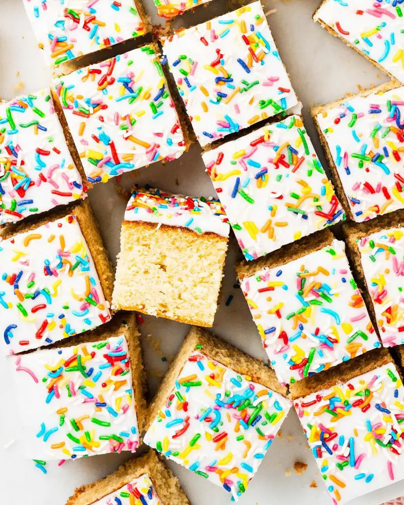 Go for gold with this nostalgic old school cake. A light vanilla traybake cake is topped with simple white icing and plenty of sprinkles. Serve with plenty of custard for the ultimate school dessert treat! Recipe by movers and bakers