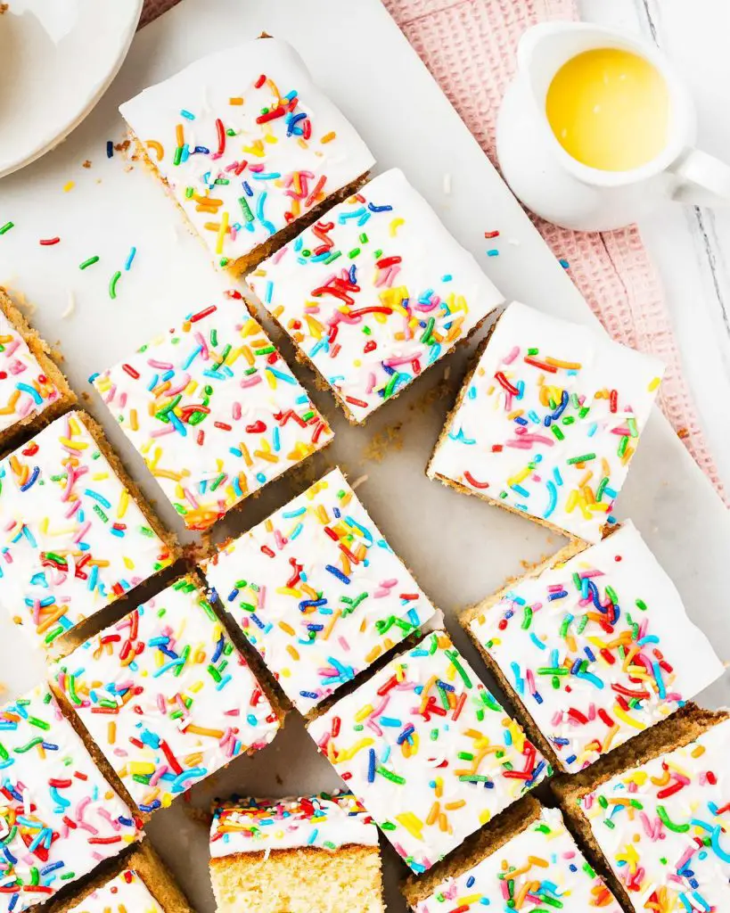 Go for gold with this nostalgic old school cake. A light vanilla traybake cake is topped with simple white icing and plenty of sprinkles. Serve with plenty of custard for the ultimate school dessert treat! Recipe by movers and bakers