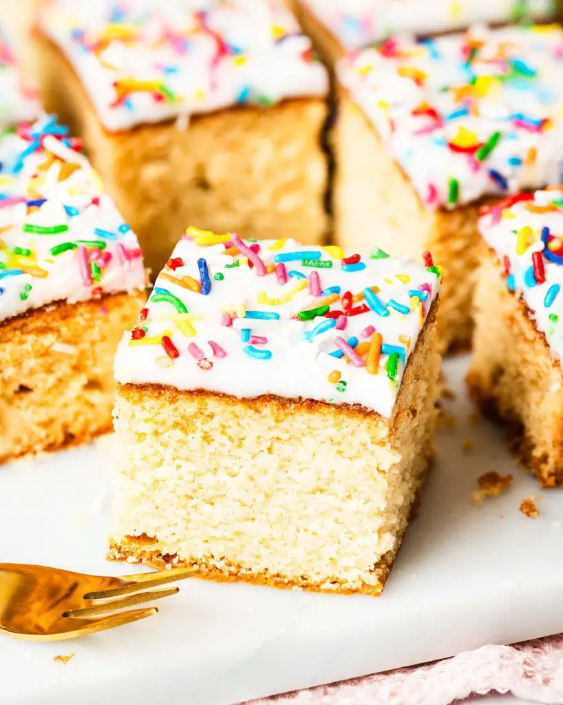 Go for gold with this nostalgic old school cake. A light vanilla traybake cake is topped with simple white icing and plenty of sprinkles. Serve with plenty of custard for the ultimate school dessert treat! Recipe by movers and bakers