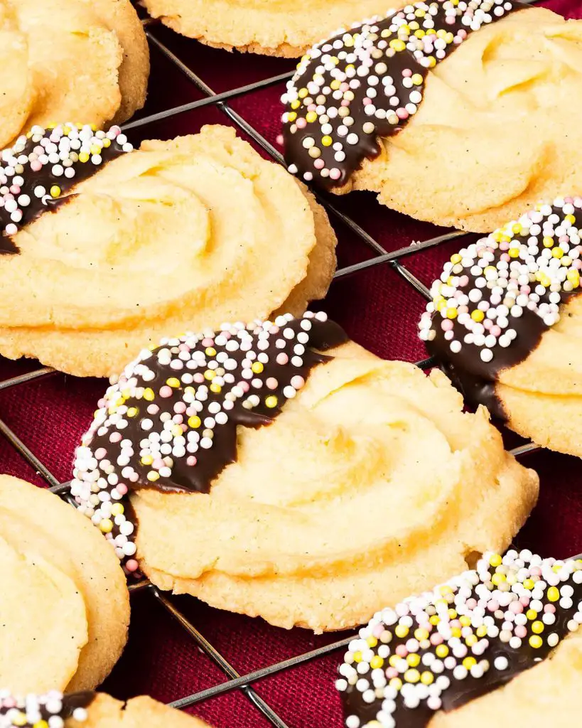 My chocolate dipped shortbread biscuits are a delightfully moreish tea time treat! Melt-in-your-mouth shortbread roses are partly dipped in chocolate and finished with colourful sprinkles for a bake everyone will love! Recipe by movers and bakers