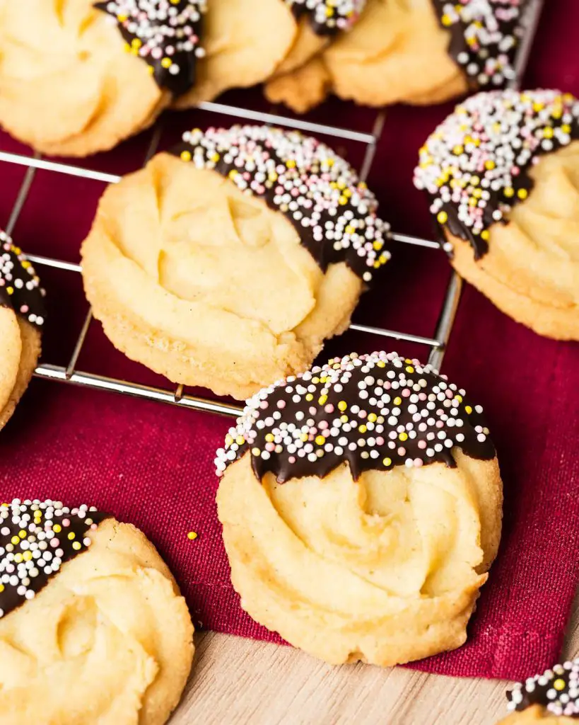 My chocolate dipped shortbread biscuits are a delightfully moreish tea time treat! Melt-in-your-mouth shortbread roses are partly dipped in chocolate and finished with colourful sprinkles for a bake everyone will love! Recipe by movers and bakers