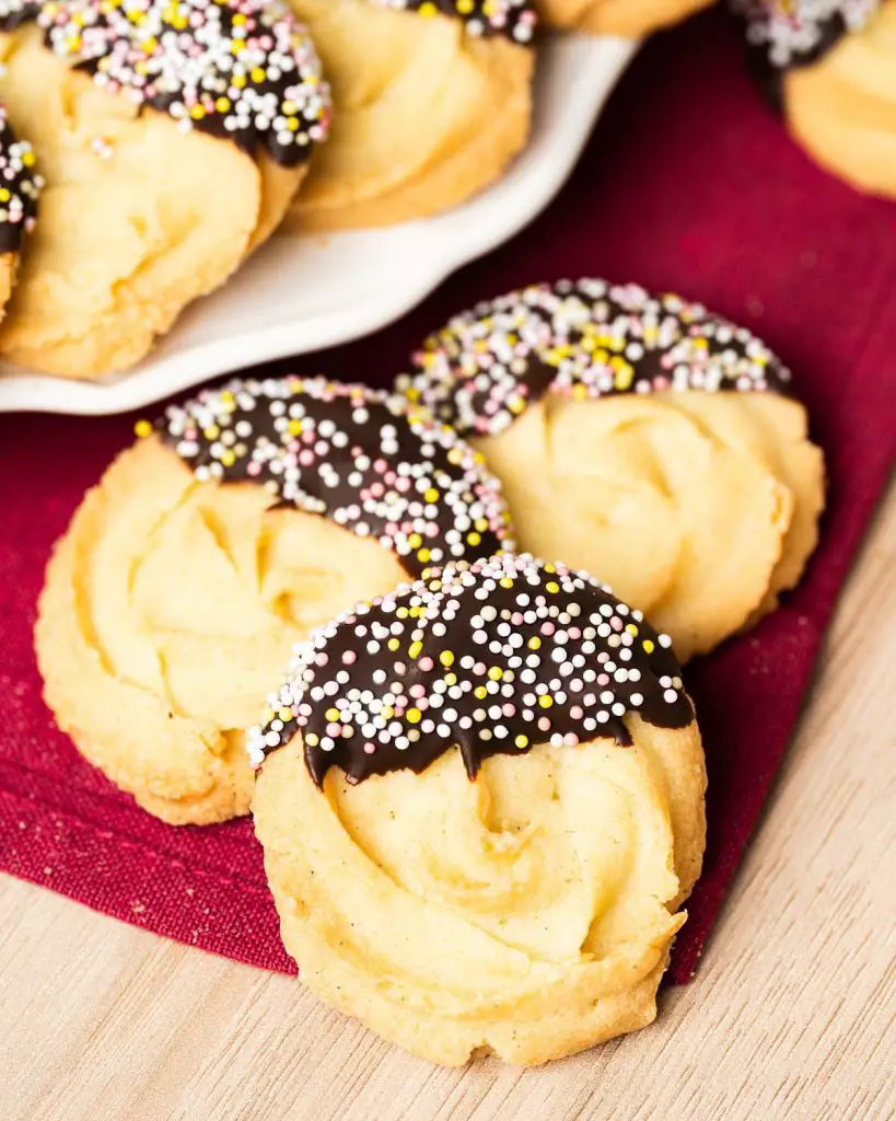 My chocolate dipped shortbread biscuits are a delightfully moreish tea time treat! Melt-in-your-mouth shortbread roses are partly dipped in chocolate and finished with colourful sprinkles for a bake everyone will love! Recipe by movers and bakers