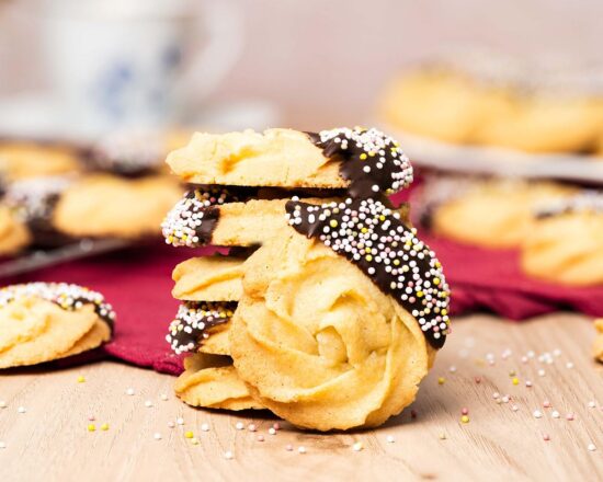 My chocolate dipped shortbread biscuits are a delightfully moreish tea time treat! Melt-in-your-mouth shortbread roses are partly dipped in chocolate and finished with colourful sprinkles for a bake everyone will love! Recipe by movers and bakers