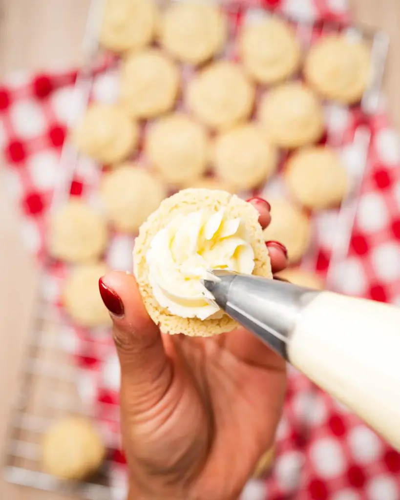 Piping buttercream on one half of the sandwich biscuits...