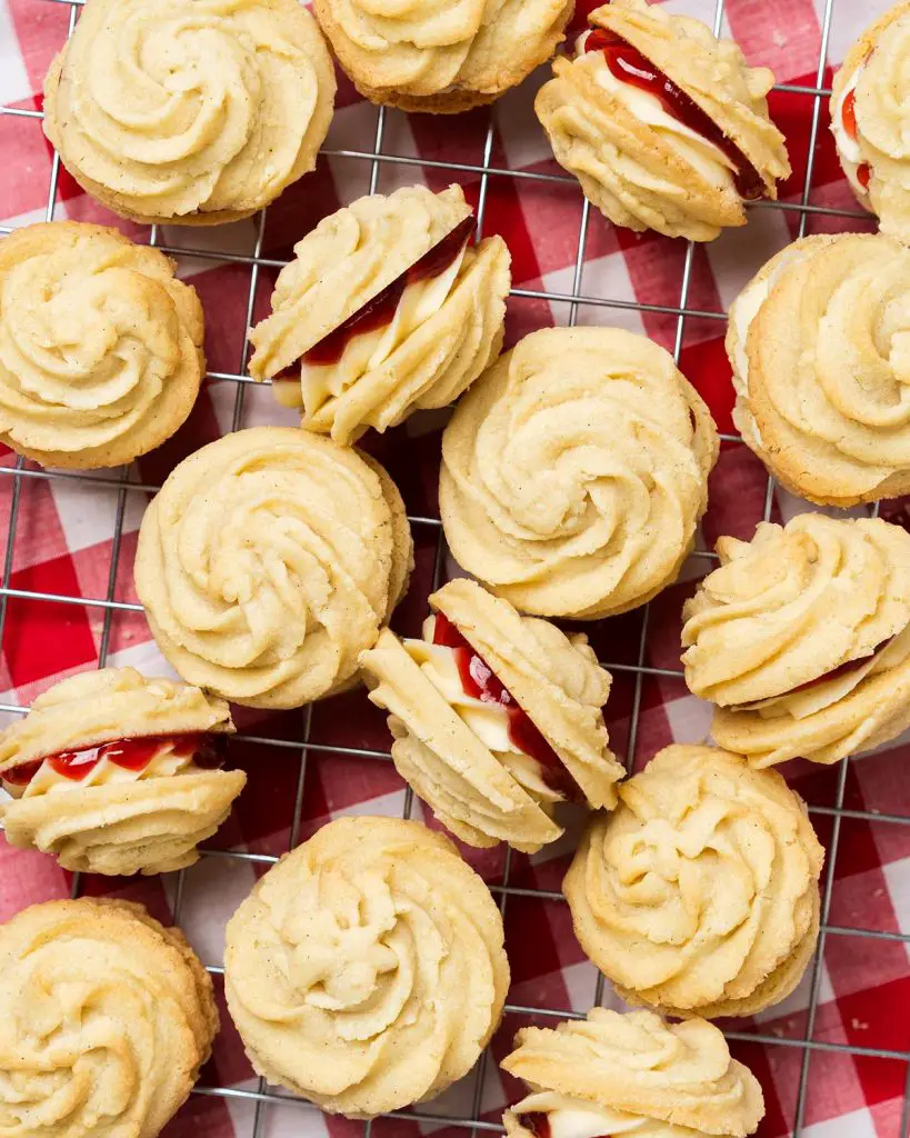 Viennese whirls are a delightful British sandwich biscuit! Two buttery piped shortbread biscuits are filled with soft vanilla buttercream and raspberry jam, making the perfect tea time treat! Recipe by movers and bakers