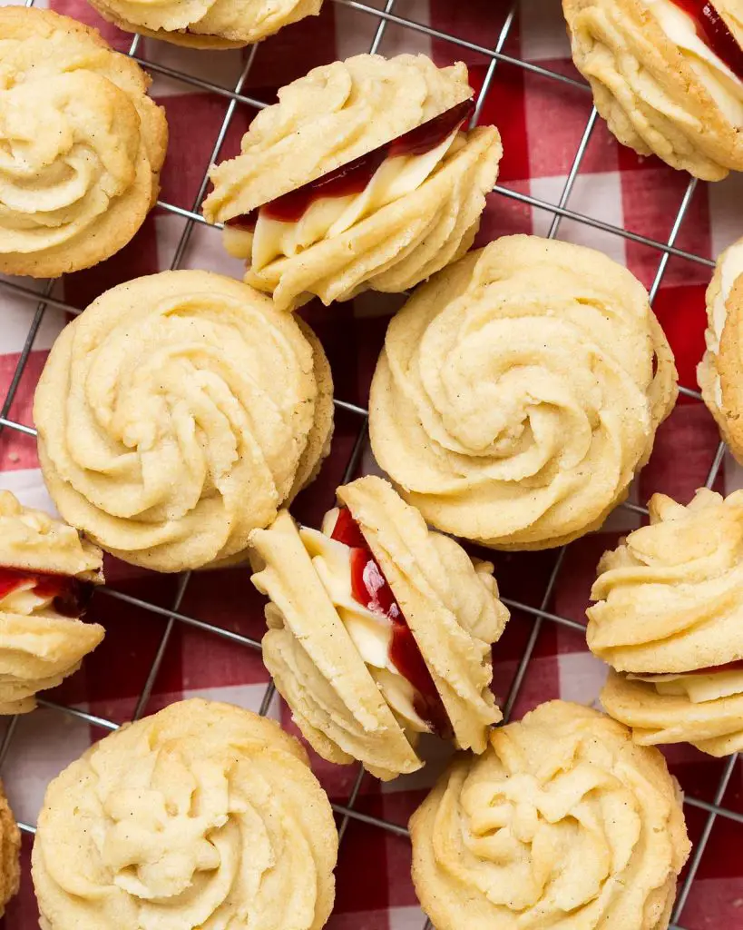 Viennese whirls are a delightful British sandwich biscuit! Two buttery piped shortbread biscuits are filled with soft vanilla buttercream and raspberry jam, making the perfect tea time treat! Recipe by movers and bakers