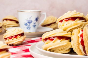 Viennese whirls are a delightful British sandwich biscuit! Two buttery piped shortbread biscuits are filled with soft vanilla buttercream and raspberry jam, making the perfect tea time treat! Recipe by movers and bakers