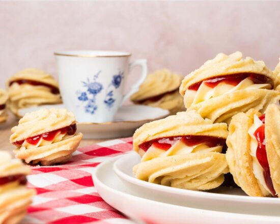 Viennese whirls are a delightful British sandwich biscuit! Two buttery piped shortbread biscuits are filled with soft vanilla buttercream and raspberry jam, making the perfect tea time treat! Recipe by movers and bakers