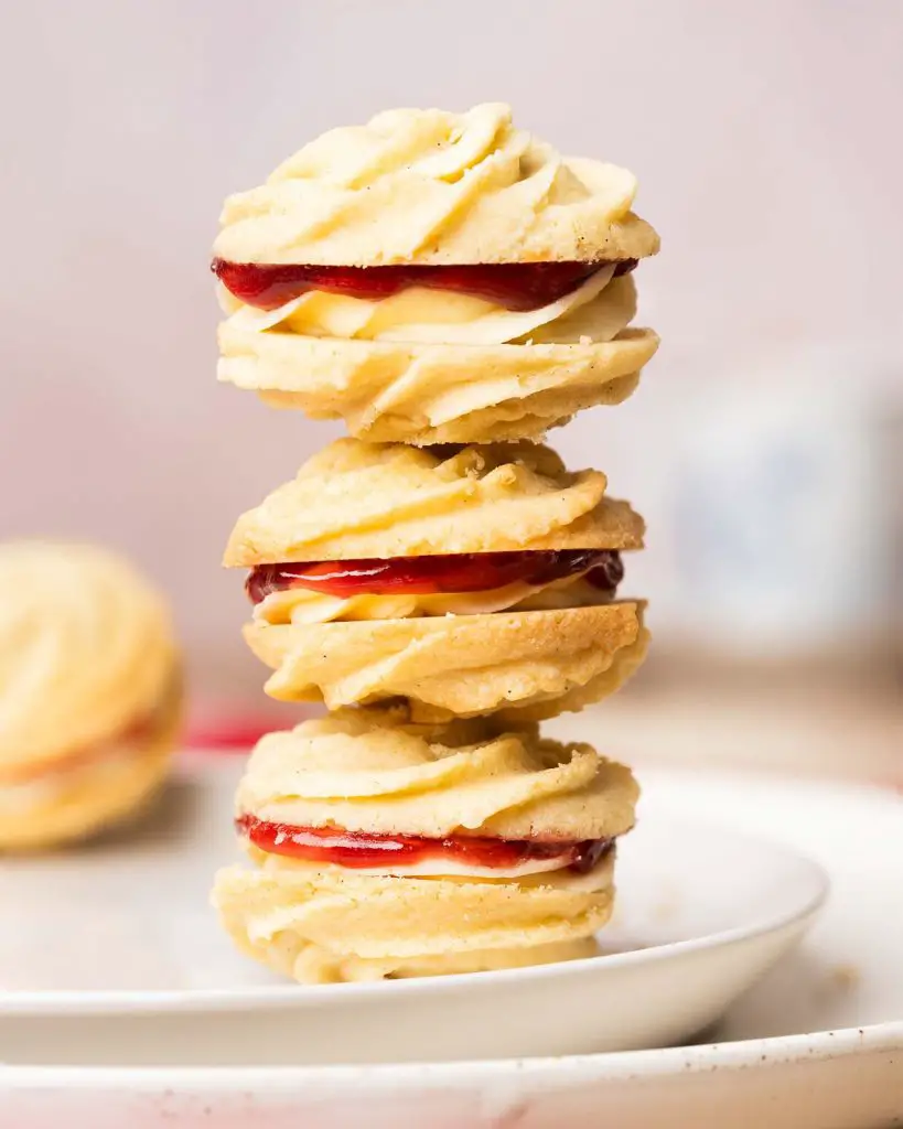 Viennese whirls are a delightful British sandwich biscuit! Two buttery piped shortbread biscuits are filled with soft vanilla buttercream and raspberry jam, making the perfect tea time treat! Recipe by movers and bakers