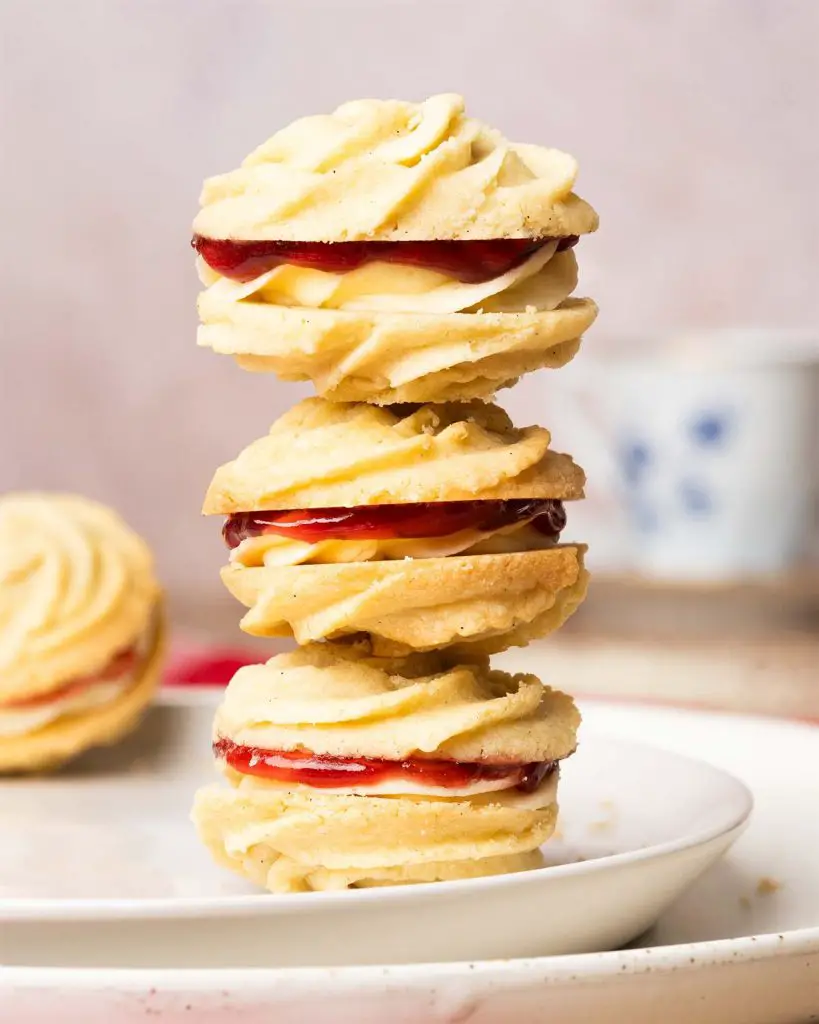 Viennese whirls are a delightful British sandwich biscuit! Two buttery piped shortbread biscuits are filled with soft vanilla buttercream and raspberry jam, making the perfect tea time treat! Recipe by movers and bakers