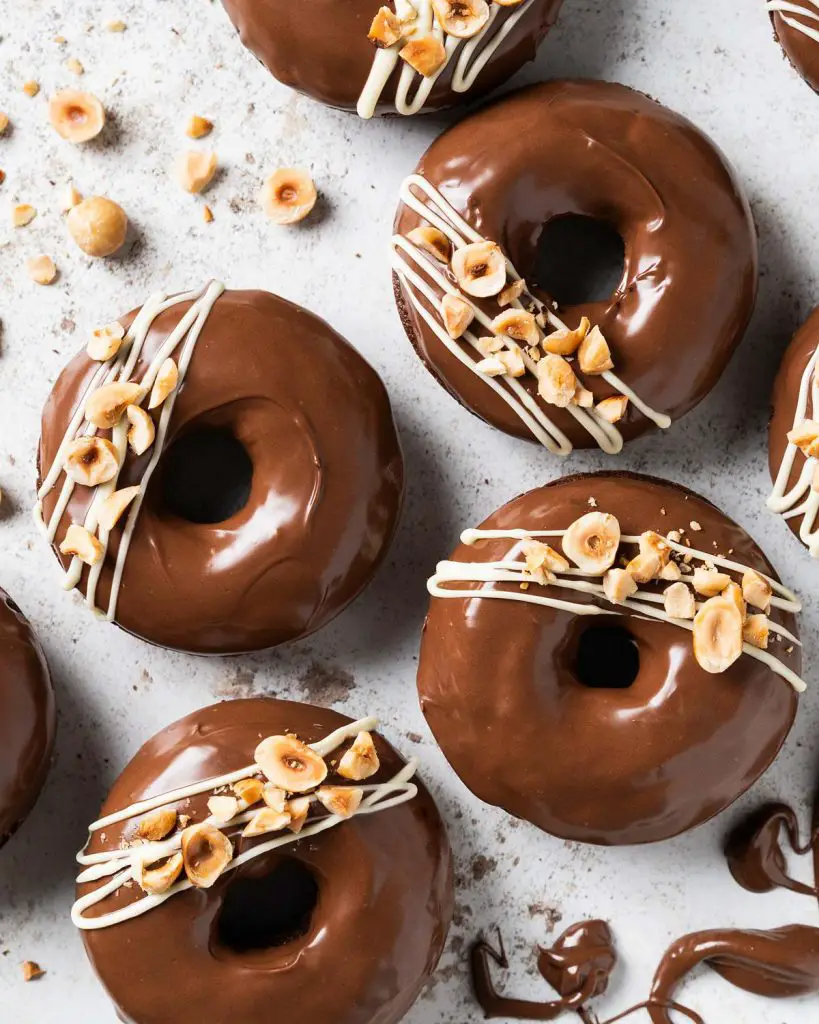 My Nutella donuts are so good, you will want to inhale more than one! A light Nutella chocolate cake baked donut is topped with smooth and glossy Nutella spread and decorated with a white chocolate drizzle and chopped toasted hazelnuts. Chocolate hazelnut heaven! Recipe by movers and bakers