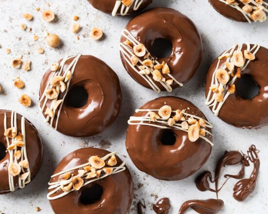 My Nutella donuts are so good, you will want to inhale more than one! A light Nutella chocolate cake baked donut is topped with smooth and glossy Nutella spread and decorated with a white chocolate drizzle and chopped toasted hazelnuts. Chocolate hazelnut heaven! Recipe by movers and bakers