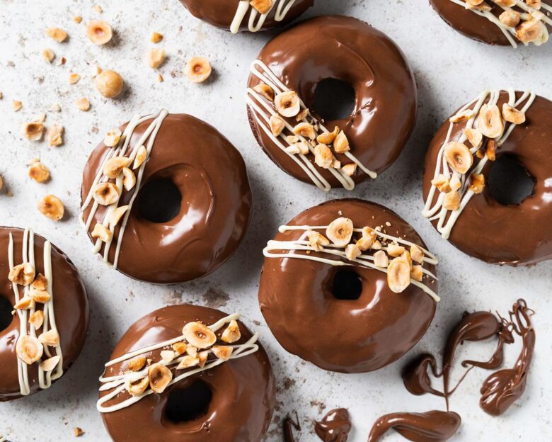 My Nutella donuts are so good, you will want to inhale more than one! A light Nutella chocolate cake baked donut is topped with smooth and glossy Nutella spread and decorated with a white chocolate drizzle and chopped toasted hazelnuts. Chocolate hazelnut heaven! Recipe by movers and bakers