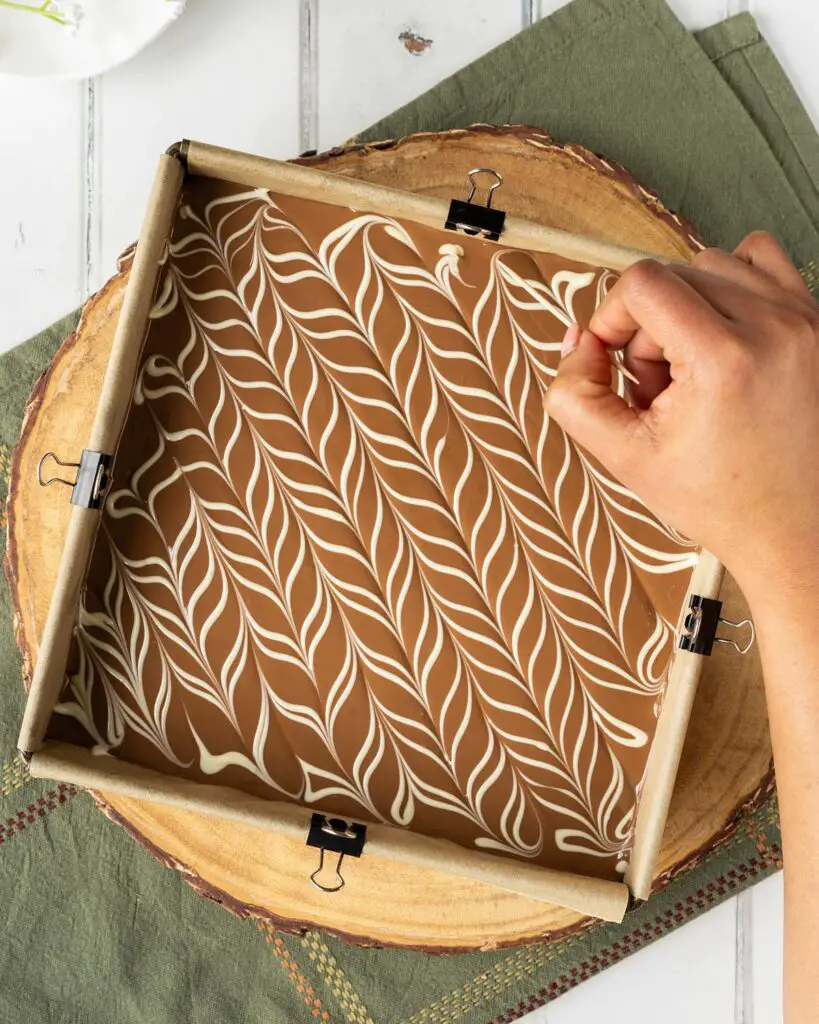 Once the milk chocolate has been smoothed over and the white chocolate piped on, use a toothpick to create the feathered effect, then leave to set. Recipe by movers and bakers