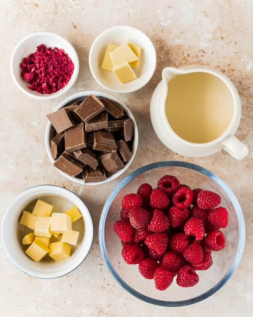 Ingredients for the filling and decoration: fresh raspberries, milk chocolate, double (heavy) cream, unsalted butter, white chocolate (optional) and freeze dried raspberries (optional). Recipe by movers and bakers