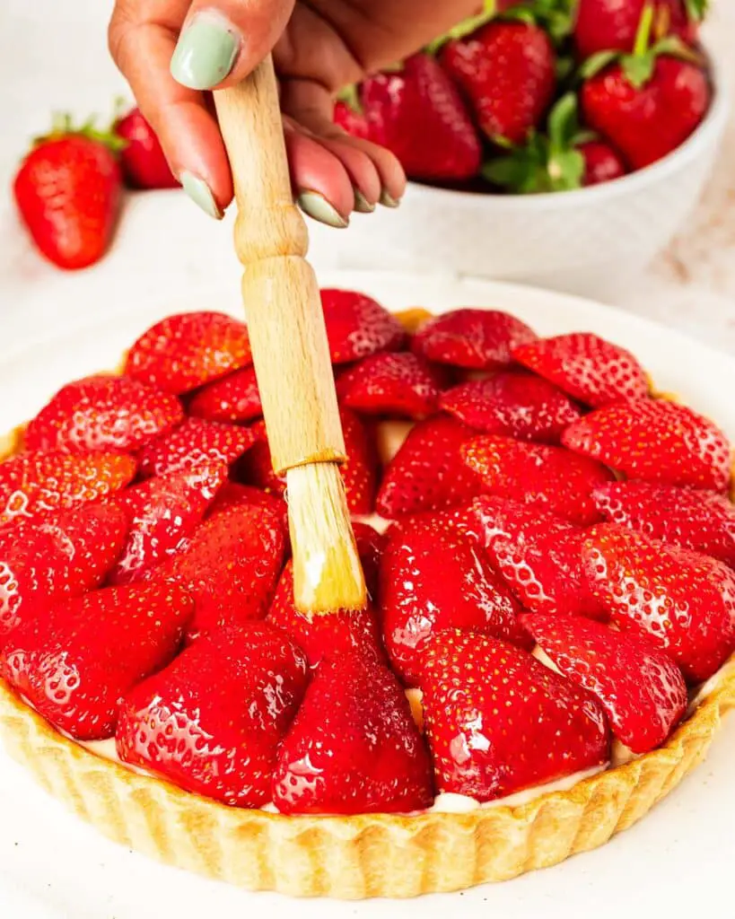 Brushing the berries with the jam for a beautiful shiny glaze. Recipe by movers and bakers