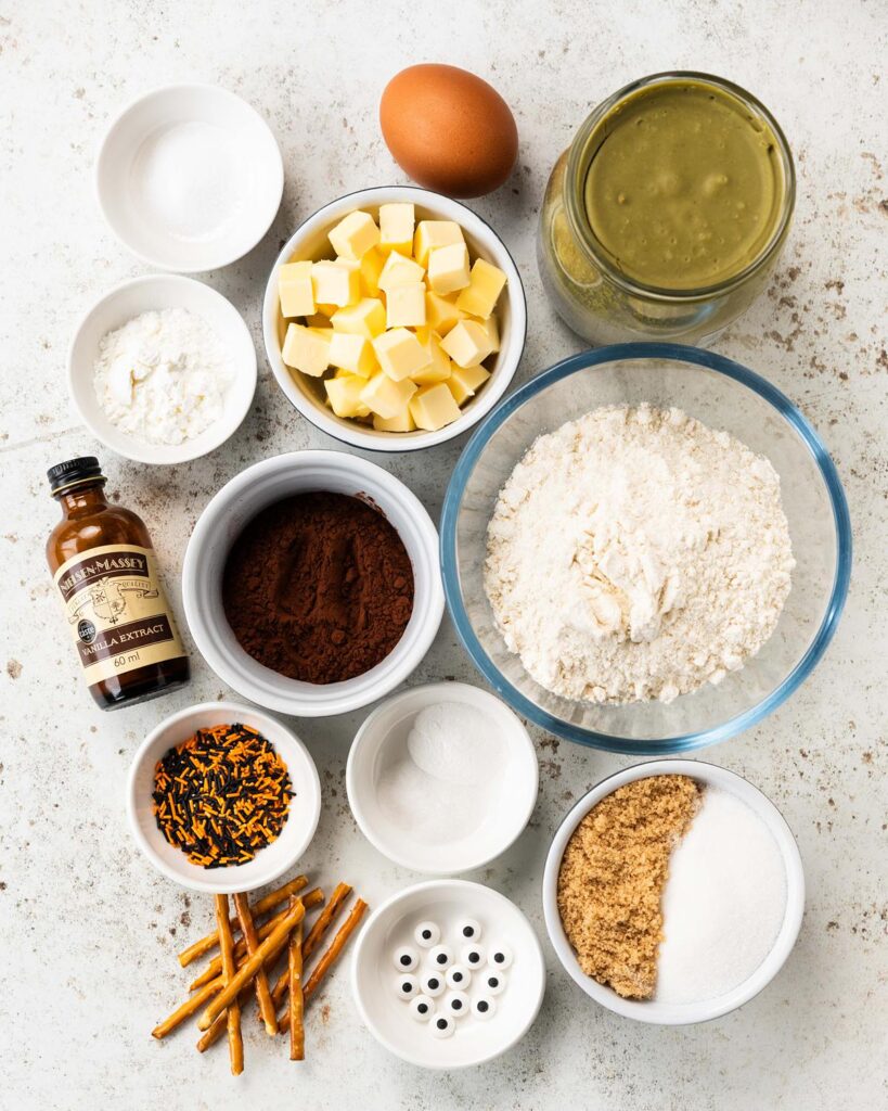 Ingredients required: unsalted butter, brown sugar, caster sugar, vanilla, plain (all purpose) flour, cocoa powder, cornflour (cornstarch), baking powder, bicarbonate of soda (baking soda), salt, an egg, pistachio cream, sprinkles and pretzel sticks. Recipe by movers and bakers