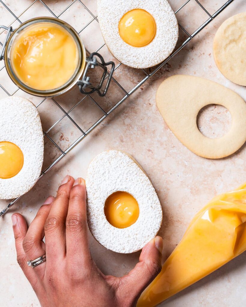 Then carefully place the matching cookie on top, gently pressing together to evenly spread out the curd filling in the Easter egg lemon curd cookies. Recipe by movers and bakers