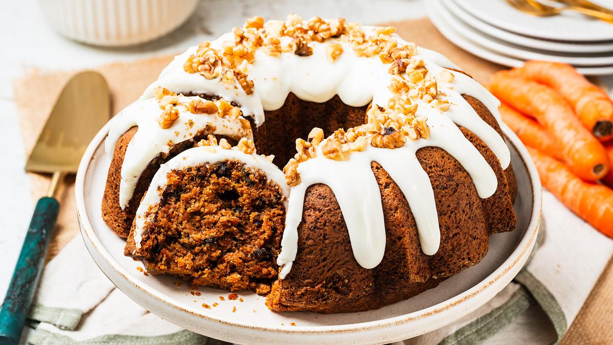 Carrot bundt cake on a cake stand with cream cheese glaze dripping into the ridges, topped with chopped walnuts. Rich, moist, perfectly spiced and totally irresistible! Recipe by movers and bakers