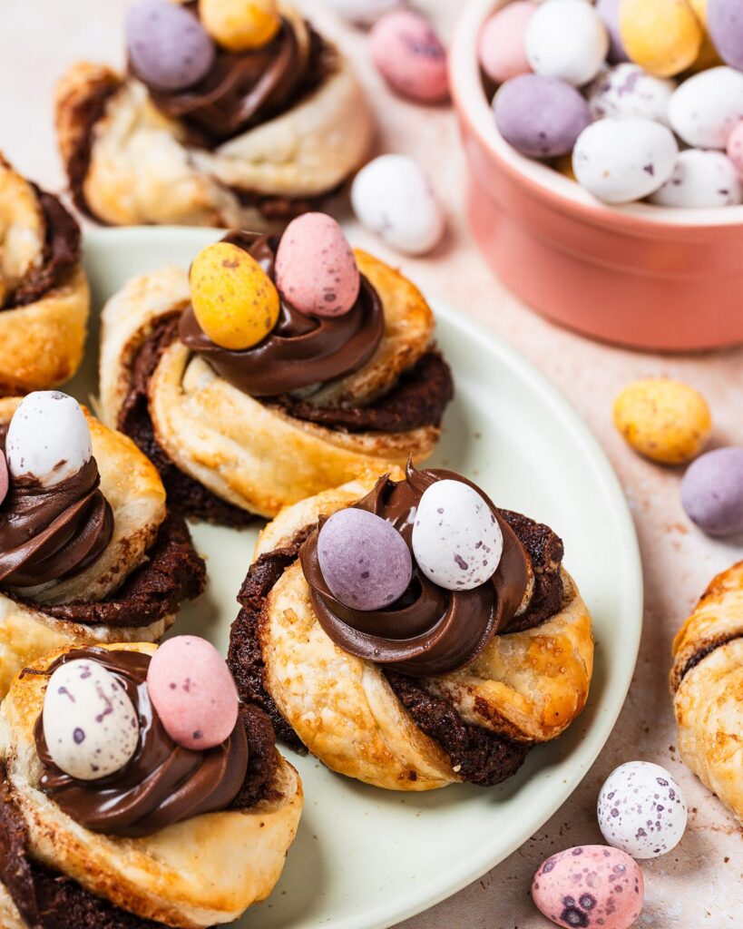 Golden, flakey, Nutella-filled pastry twists, curled into nests and topped with more Nutella and mini eggs, these puff pastry Easter nests are everyone's favourite! Recipe by movers and bakers