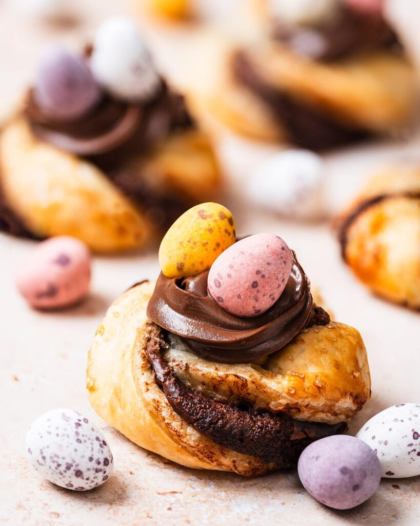 Golden, flakey, Nutella-filled pastry twists, curled into nests and topped with more Nutella and mini eggs, these puff pastry Easter nests are everyone's favourite! Recipe by movers and bakers