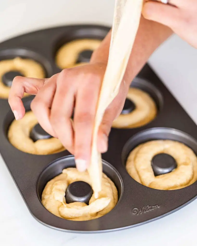 Piping the doughnut batter into the doughnut pan before baking.