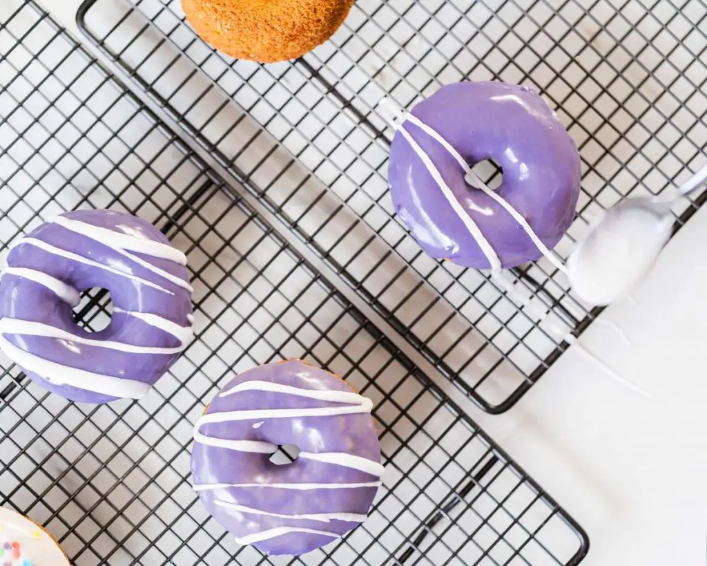 The purple glazed doughnuts being drizzled with a beautiful thick white glaze drizzle.