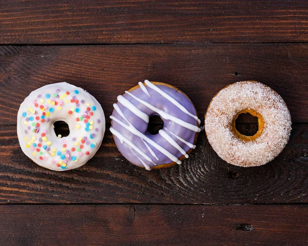 A trio of beautiful light and fluffy baked doughnuts: one covered with sprinkles, one with a glorious purple glaze with white drizzle and the third coated in crunchy sugar. Which would you pick?