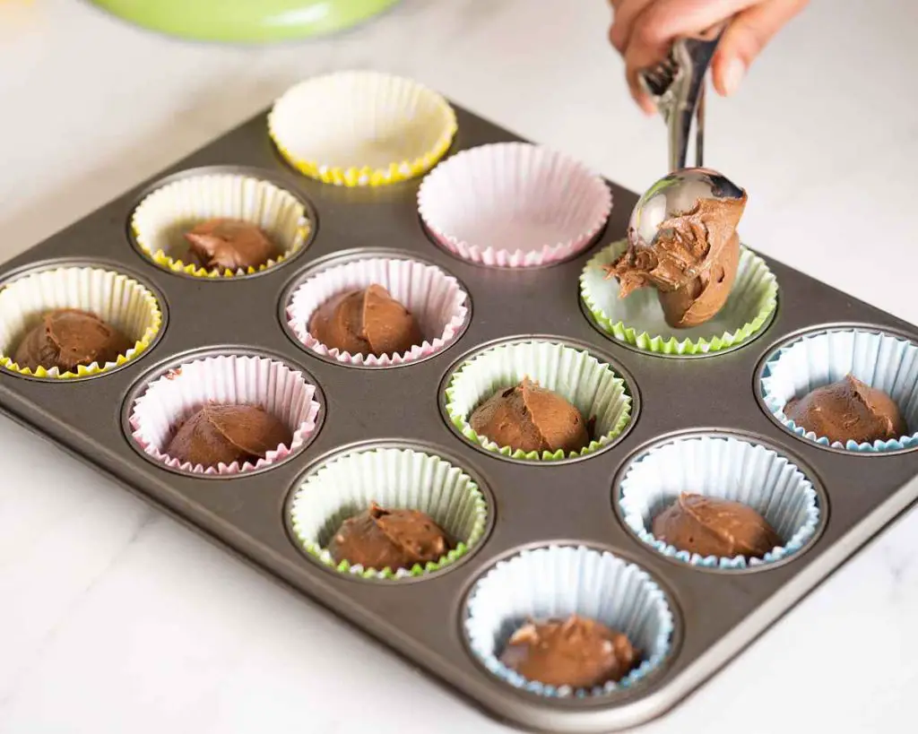 Spooning chocolate cake mixture into cupcake cases before baking. Recipe by movers and bakers