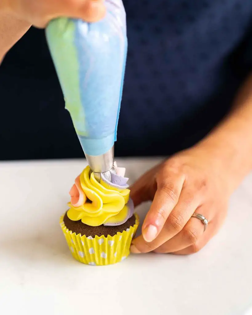 Piping a chocolate cupcake with the colourful vanilla buttercream. Recipe by movers and bakers