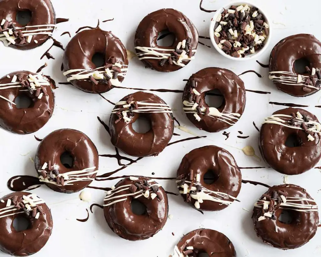 An overhead view of a selection of chocolate fudge doughnuts with drizzles of fudge icing and white chocolate for decoration.